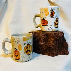 two coffee mugs decorated with jack - o'- lanterns are sitting on a piece of wood