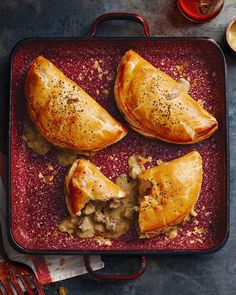 three pieces of meat filled pastries on a red platter next to silverware and utensils