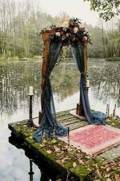 an outdoor ceremony setup with blue draping and flowers on the ground, surrounded by water