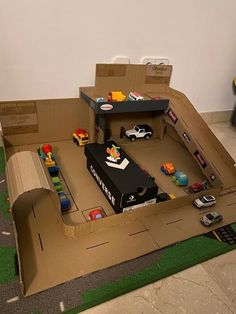 an open cardboard box with toy cars and trucks in it on the floor next to a wall