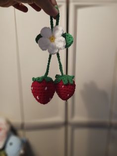 crocheted strawberry ornament being held by someone's hand with white flower