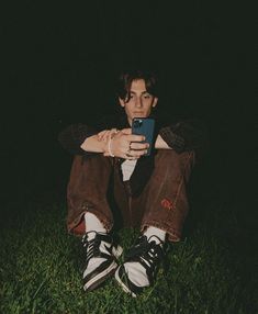 a man sitting in the grass looking at his cell phone