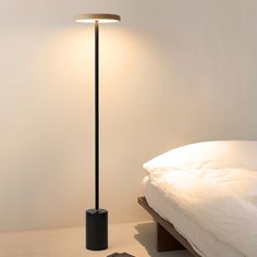 a floor lamp next to a bed in a room with white walls and tile floors