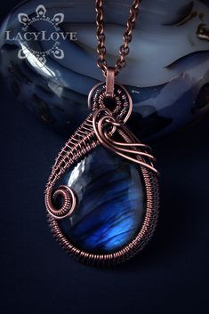 a wire wrapped pendant with a blue stone in the shape of a tear on a black background