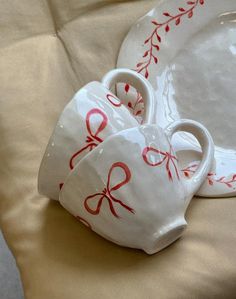 two white dishes with red bows on them are sitting on a beige cloth covered tablecloth