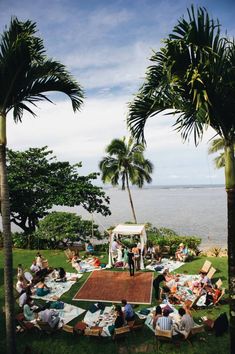 people are sitting on lawn chairs and tables near the water with palm trees in the foreground