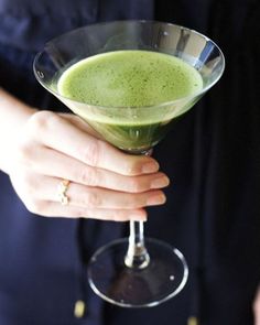 a close up of a person holding a drink in a wine glass with green liquid