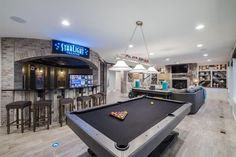 a pool table in the middle of a room with bar stools and television on the wall