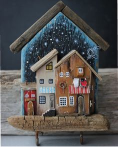 a small wooden house sitting on top of a piece of wood with snow falling off the roof