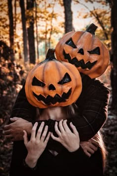 two people with pumpkins on their heads hugging in the middle of an autumn forest