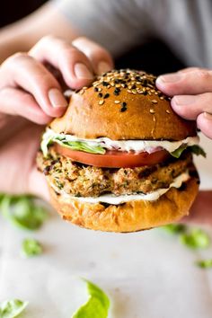 a person holding a hamburger with lettuce and tomato on it in their hands