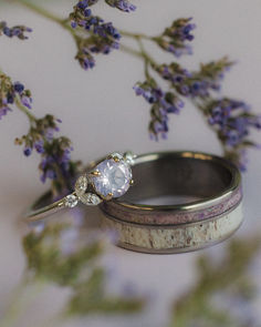 A matching purple wedding ring set from Staghead Designs sits on pastel purple paper surrounded by purple flowers. This ring set features our "Blossom" design engagement ring in 14K white gold with a round lavender quartz center stone and marquise and round floral diamond accents. Below sits our "Raptor" men's wedding band with a two channel design featuring antler and sugilite and fire and ice opal mixed inlays. Staghead Designs Engagement Rings, Floral Wedding Ring Set, Whiskey Barrel Wedding Ring, Antler Wedding Rings, Matching Wedding Ring Sets, Antler Wedding Band, Matching Ring Set, Dream Rings, Pretty Engagement Rings