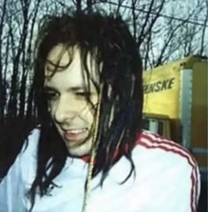 a man with long hair and dreadlocks standing in front of trees