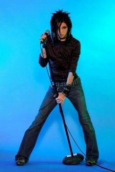 a man with black hair holding a microphone and standing on a blue background in front of the camera