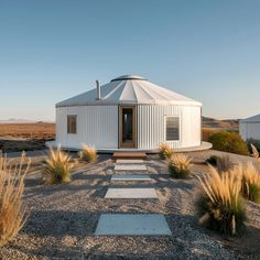 a small white house in the desert surrounded by dry grass and grasses, with a walkway leading up to it