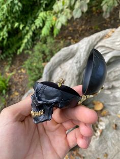 a hand holding a black object with a skull on it's side and two other objects in the background