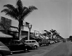 an old black and white photo of cars parked on the side of the road in front of shops