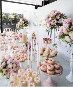 a table topped with lots of donuts covered in frosting next to tall vases filled with flowers