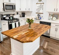 a kitchen with white cabinets and wood counter tops, stainless steel appliances and an island in the middle