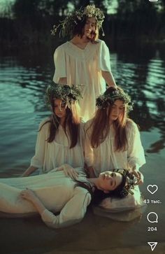 three women with wreaths on their heads sitting in the water