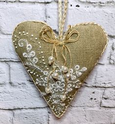 a heart shaped decoration hanging from a string on a brick wall with pearls and lace