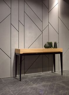 a wooden table with two vases on it in front of a wall that has geometric designs