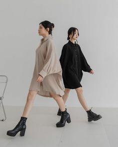 two women in black and beige outfits walking down a white floor next to each other