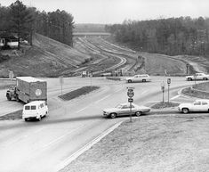 an old black and white photo of cars driving down a road with construction in the background