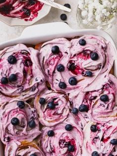 blueberry rolls in a white baking dish with whipped cream and blueberries on top