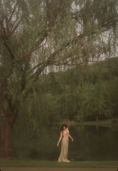 a woman standing in front of a tree next to a lake