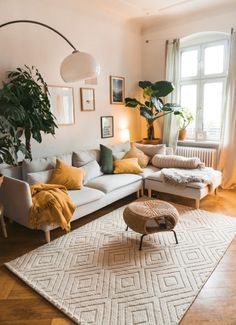 a living room filled with lots of furniture and plants on top of a rug in front of a window