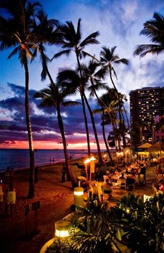 the beach is lined with palm trees and lit up tables at night, while the sun sets