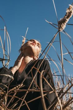 a woman standing in tall grass with her hand on her ear and looking up into the sky