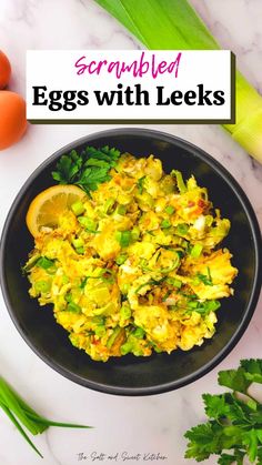 scrambled eggs with leeks in a black bowl on a marble table next to fresh vegetables