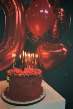 a birthday cake with lit candles and balloons in the shape of heart shaped balloons on a table