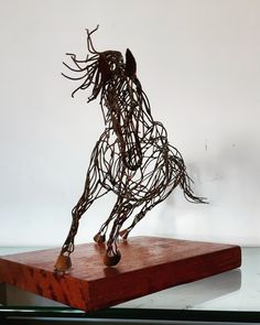 a sculpture of a horse made out of wire on top of a wooden block in front of a white wall