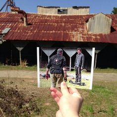 a hand holding up a photo of two men in front of a rusted building