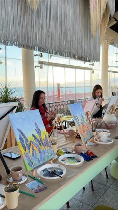 two women sitting at a table with paintings on it