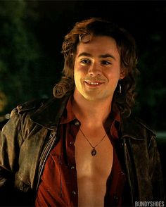 a man with long hair wearing a leather jacket and red shirt smiling at the camera