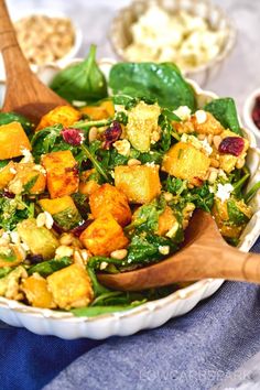 a salad with spinach, pine nuts and cranberries in a white bowl