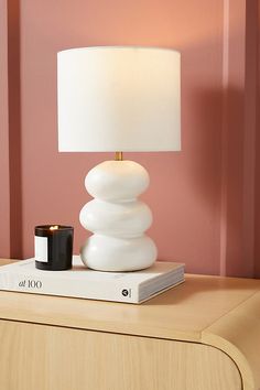 a white lamp sitting on top of a wooden table next to a book and cup