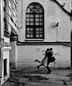 black and white photograph of a man running in front of a building with an umbrella