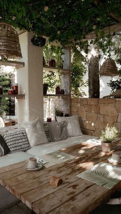 a wooden table sitting under a tree next to a wall filled with potted plants