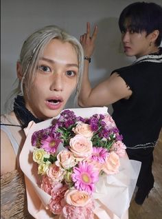 a woman holding a bouquet of flowers in front of her face and another person standing behind her