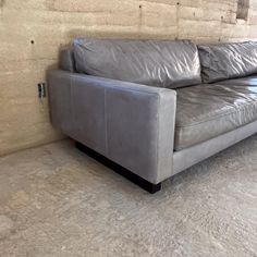 a gray leather couch sitting on top of a floor next to a brick wall in an empty room