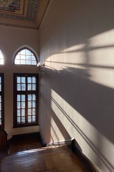 an empty room with three arched windows and wooden floors in the center, on which there is a staircase leading up to it