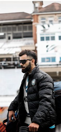 a man with a beard wearing sunglasses and a puffy jacket walks down the street