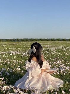 a woman sitting in the middle of a field with white flowers on it's grass