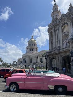 an old pink convertible car parked in front of a building with a dome on top