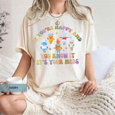 a woman is sitting on her bed holding a coffee mug and wearing a t - shirt that says you're happy and you know it, its your kids